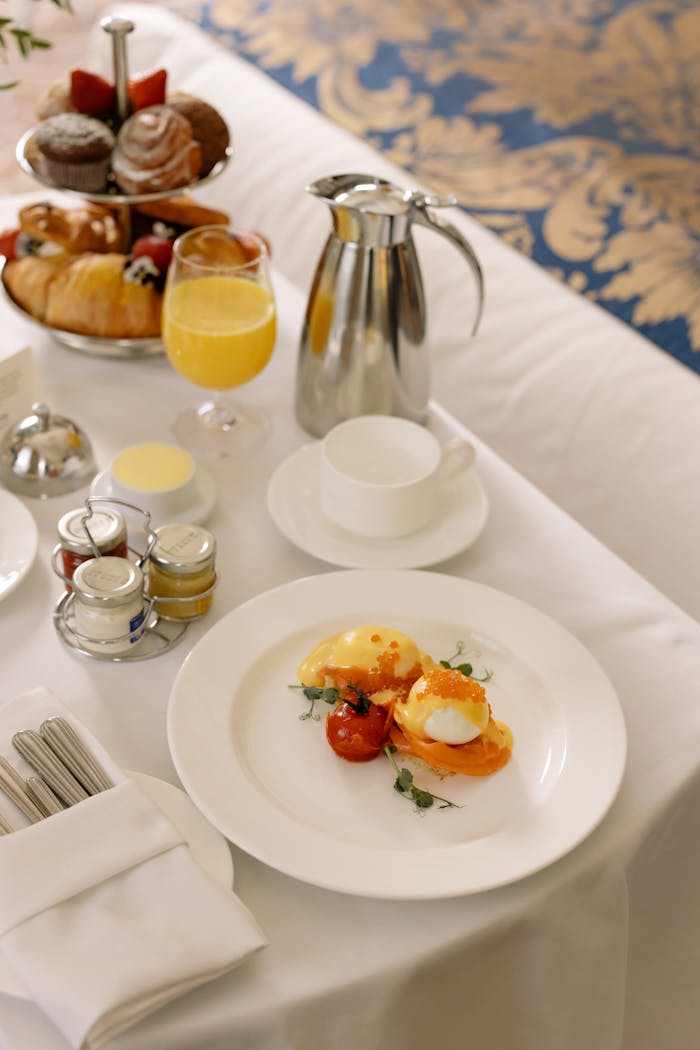 Luxurious hotel breakfast service featuring poached eggs, pastries, and orange juice elegantly arranged indoors.